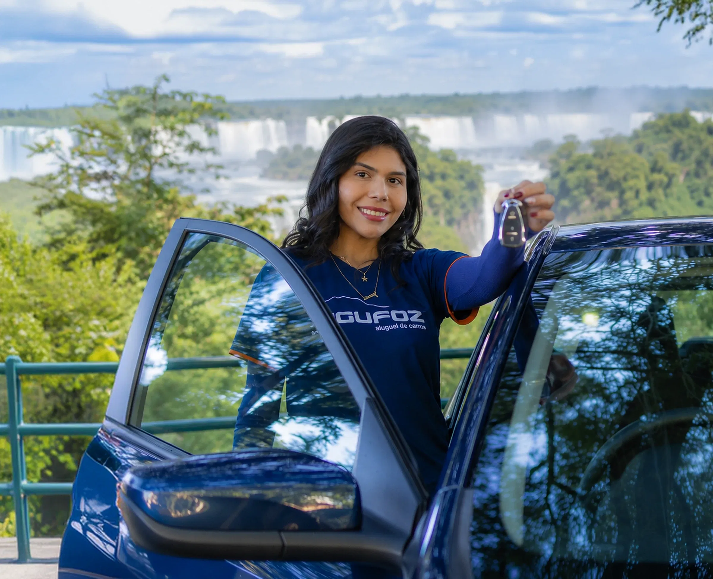 Atendente da IguFoz segurando a chave de um carro, com as Cataratas do Iguaçu ao fundo